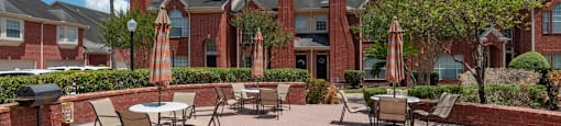 A patio with tables and chairs is surrounded by a brick wall and palm trees.