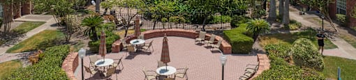 A courtyard with tables and chairs surrounded by green bushes and trees.