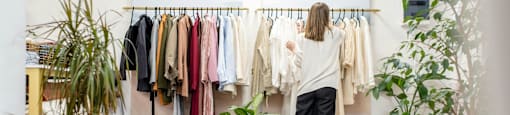 A woman is looking at clothes on a rack in a room with potted plants.