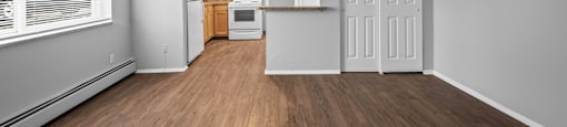 the living room and kitchen of an apartment with wood flooring and a large window