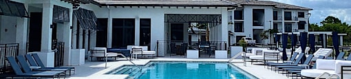 a swimming pool in front of a hotel with chairs and a blue sky