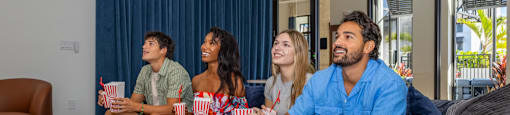 Four people sitting on a couch eating popcorn.
