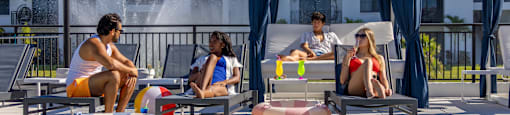 Four people are sitting by a pool with a waterfall in the background.
