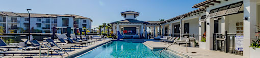 A sunny day at the pool with chairs and buildings in the background.