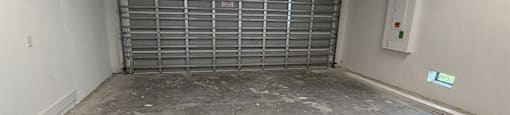 A garage with a closed metal gate and a concrete floor.