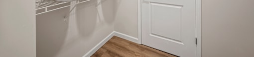 A white pantry with a white door and shelves with bowls on them.