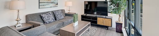 A living room with a grey couch and a painting on the wall.
