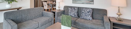 A living room with a grey couch and a painting on the wall.
