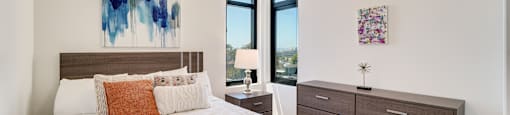 A bedroom with a large bed, a nightstand with a lamp, and two pieces of artwork on the wall.