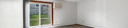 A room with a carpeted floor and a sliding glass door leading to a balcony.