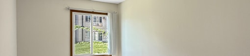 A room with a carpeted floor and a window showing a view of a building outside.