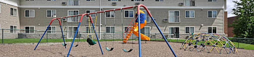 A playground with swings and slides in front of a building.