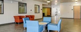 A community lobby with blue and orange chairs and tables.