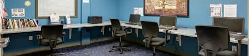 A room with blue walls and a carpeted floor has several chairs and desks arranged in rows.