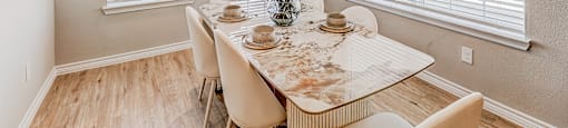 A dining room with a table set for two and a vase of red flowers.