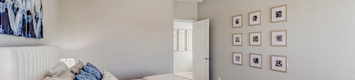 A bedroom with a bed, pillows, a ceiling fan, and pictures on the wall.