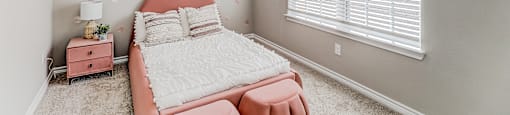 A bedroom with a pink bed and a white bedspread.