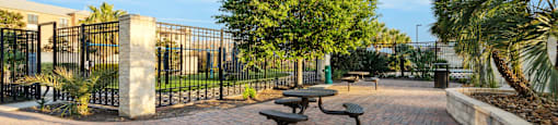 A brick walkway leads to a gate with a tree in the background.