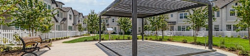 a park with a bench and a canopy in front of some apartments
