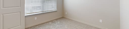 A room with a carpeted floor and a window with blinds.