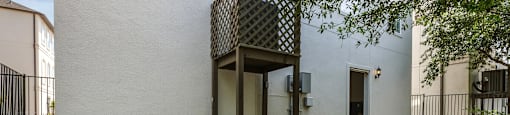 A white building with a black gate and a tree in front.
