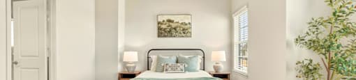 A bedroom with a bed, two lamps, a ceiling fan, and a potted plant.