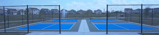 A tennis court with a blue surface and white lines is surrounded by a black fence.