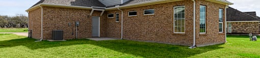 A house with a grey roof and a brick exterior sits in a grassy field.
