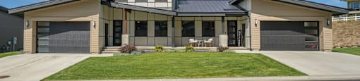 A modern duplex residence with a front yard, two driveways, and two garage doors.