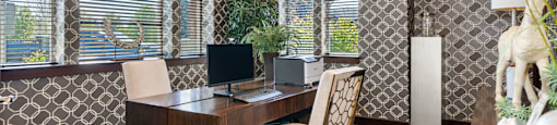 A room with a computer, printer, desk, and chairs with patterned wallpaper.