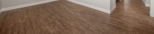 A room with wooden floors and a kitchen area behind it.