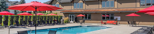 A pool area with red umbrellas and chairs in front of a building.