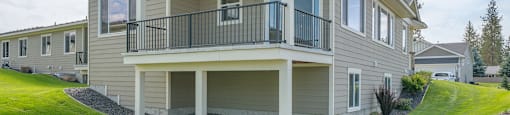 A two-story house with a balcony, a backyard and a stone wall in front.