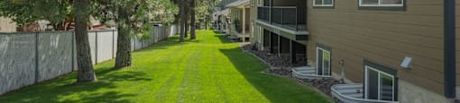 A long, narrow lawn leads to a building with a balcony.