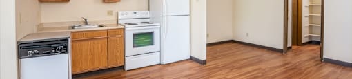 an empty kitchen with white appliances and wood floors