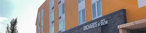 A modern building with the sign "Orchards of 82ND" on its facade.