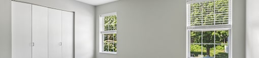 A room with grey carpet and a window with blinds.