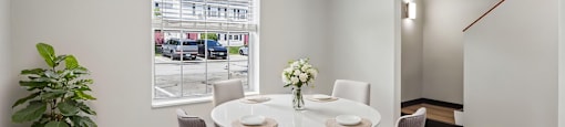 A dining room with a table set for four and a view of a parking lot outside the window.