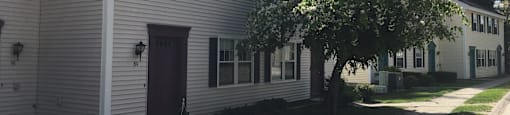 A white building with a red door and a tree in front.