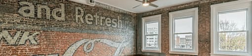 an empty room with wood floors and a brick wall with a mural on it that says and