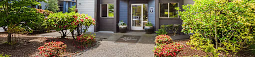 the front of a grey building with a walkway and plants at Eagles Landing Apartments, Everett, 98204