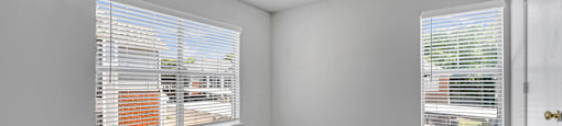 an empty living room with two windows and carpeting at Villas of Sorrento Apartments, Texas
