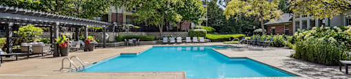 A pool surrounded by lounge chairs and trees.