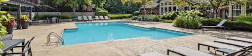 A pool surrounded by lounge chairs and trees.