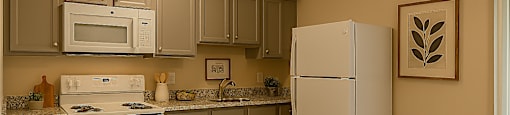 A kitchen with a white refrigerator and a white stove with a yellow towel on it.
