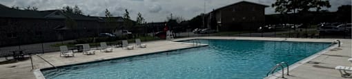 A large outdoor swimming pool with sun loungers and a cloudy sky.