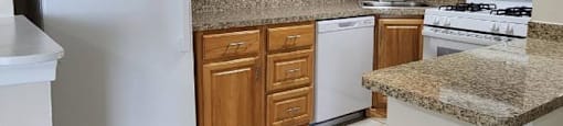 A kitchen with a white refrigerator, brown cabinets, and a granite countertop.