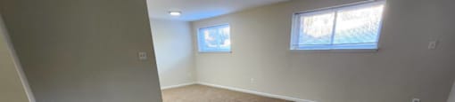 A room with carpeted floor and two windows.