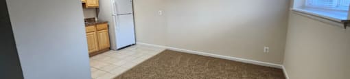 A room with a carpeted floor and a white refrigerator.