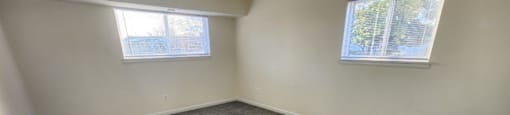 A room with grey carpet and two windows.